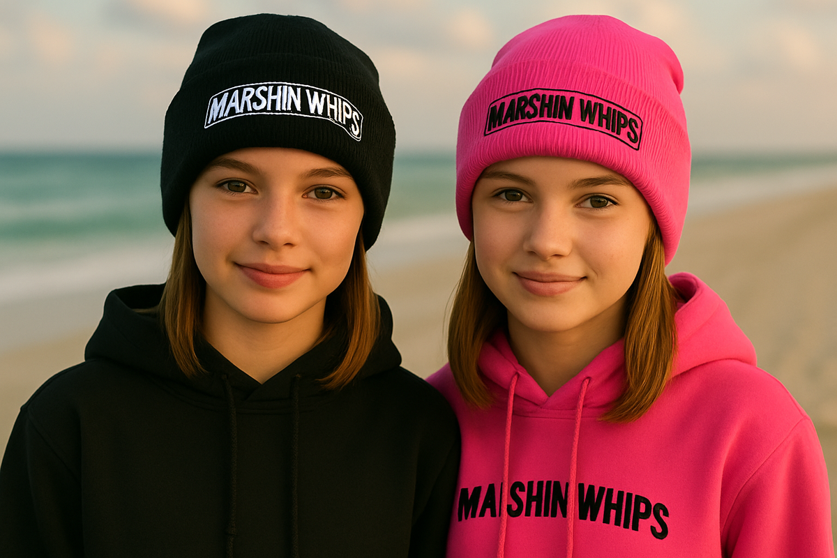 Two people wearing black and pink hoodies with 'MARSHIN WHIPS' text on a beach.