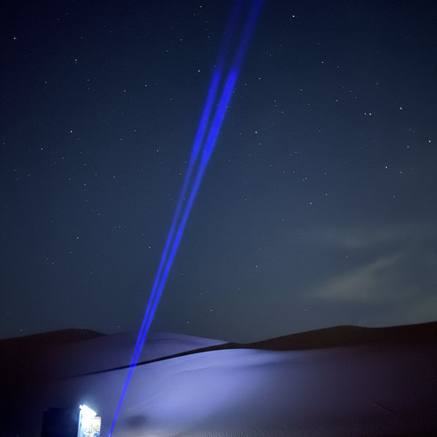 Blue laser pointer beam against a night sky with trees