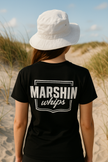 Person wearing a black t-shirt with 'MARSHIN whips' text on a beach